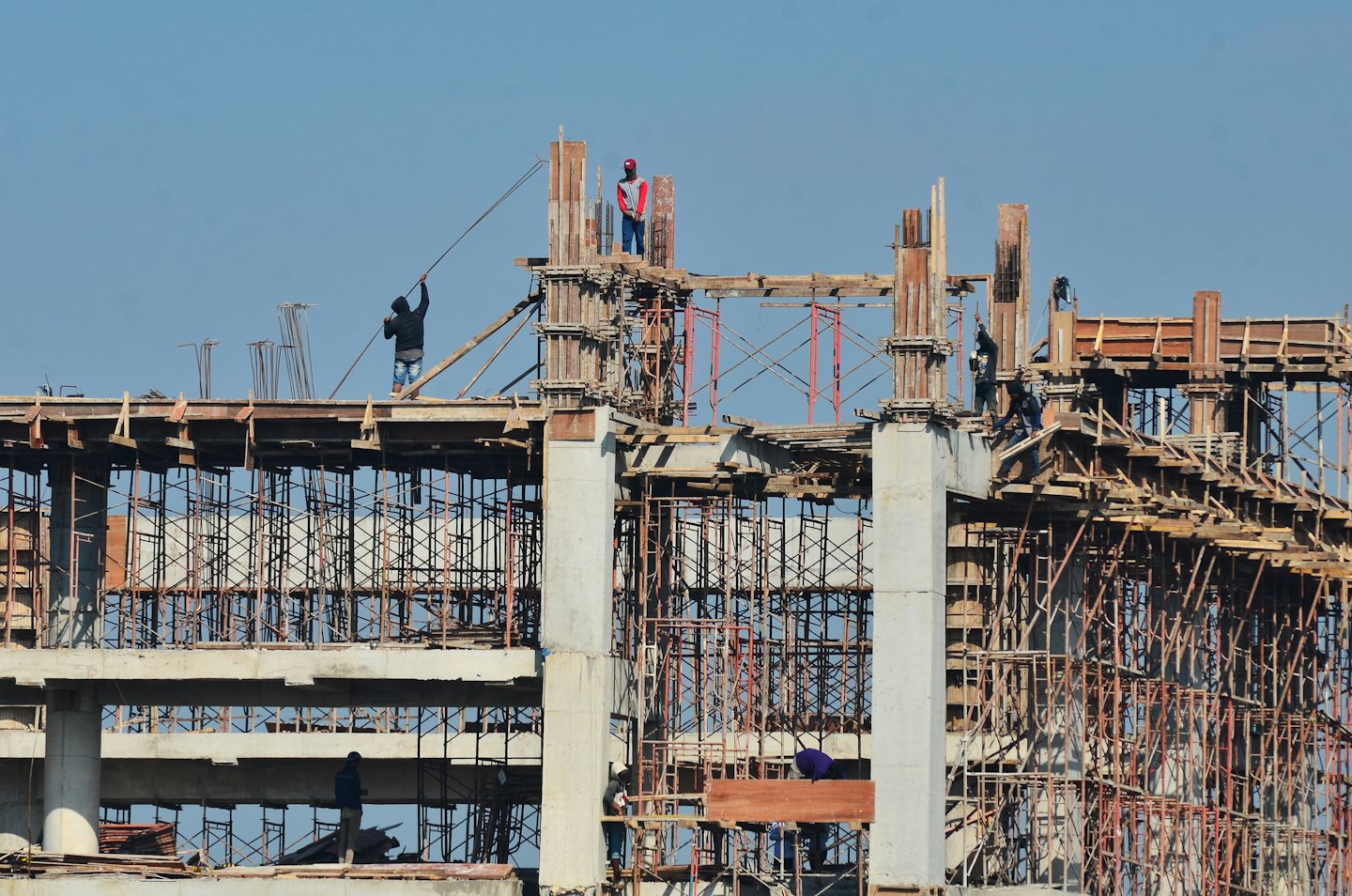 Construction workers build a large concrete structure with metal scaffolding.