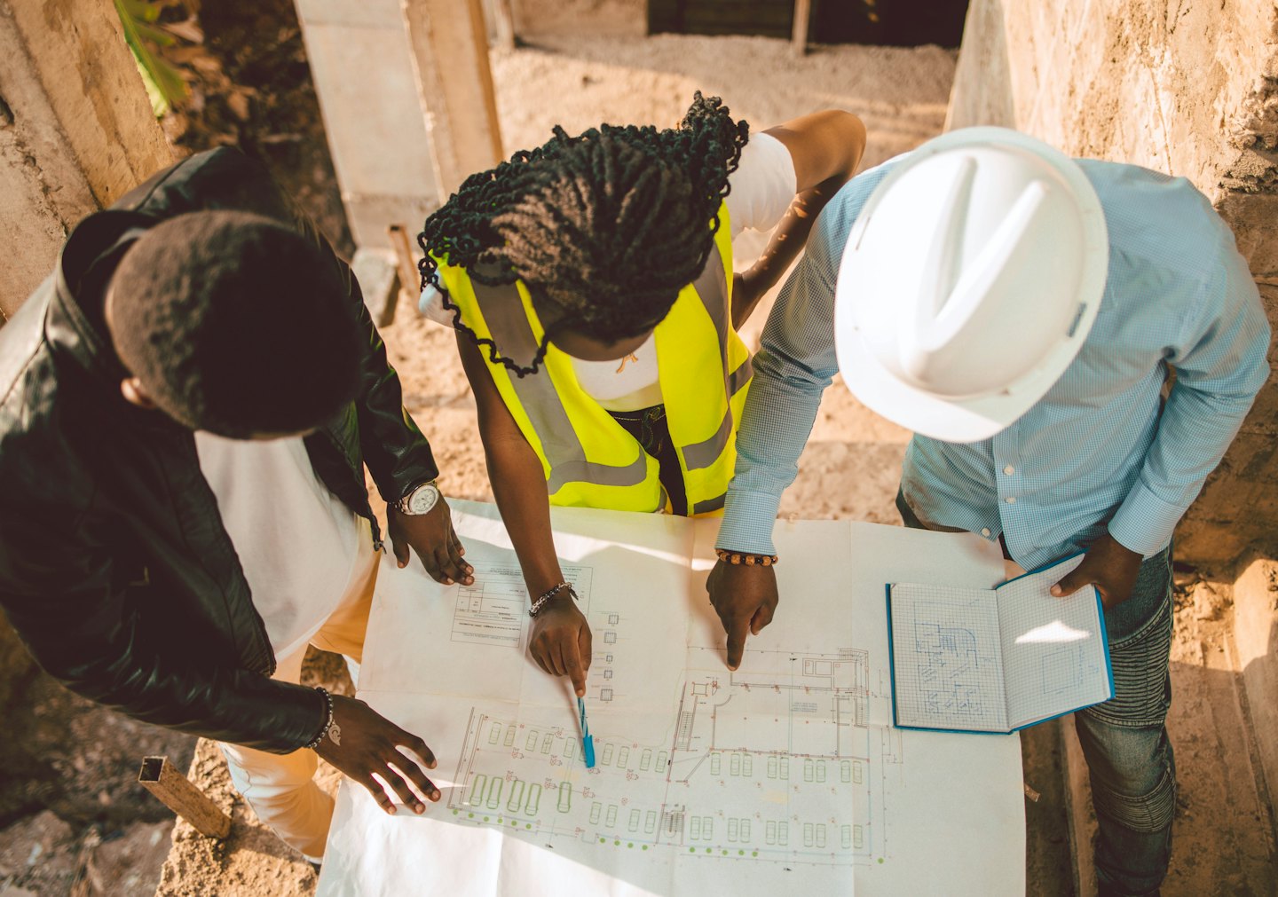 Three construction professionals review blueprints on a concrete site.